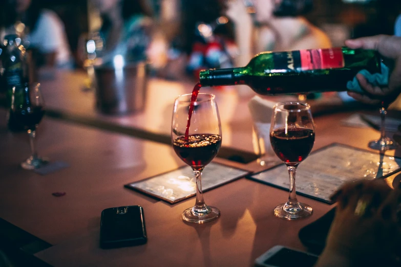 a person pours wine into two glasses