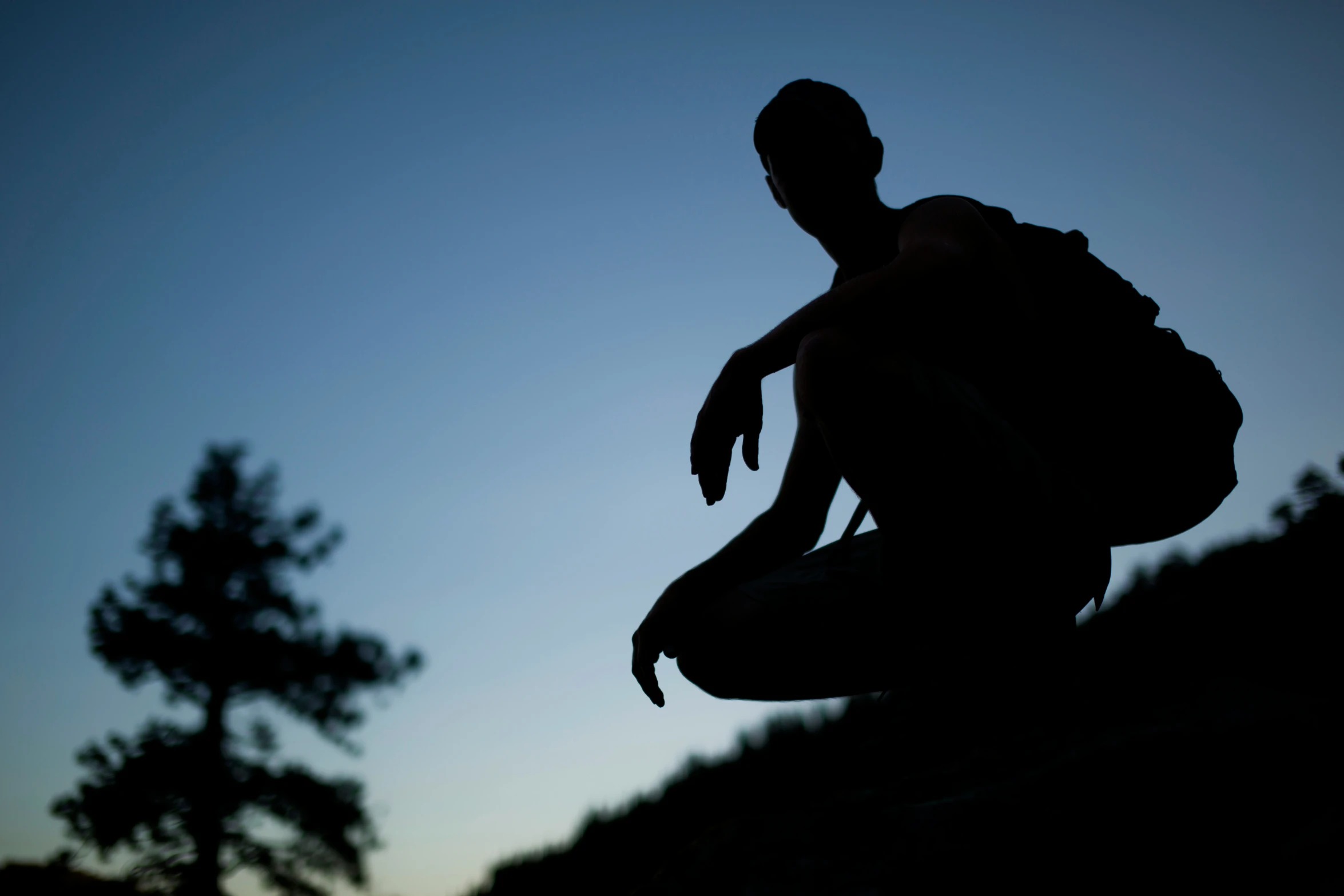 the silhouette of a man with a backpack is seen against a dusk sky