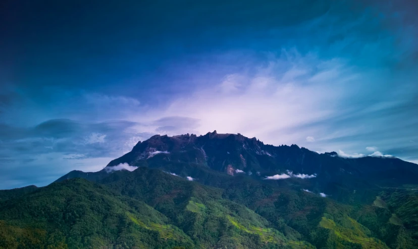 a very tall mountain is seen with the clouds in the air