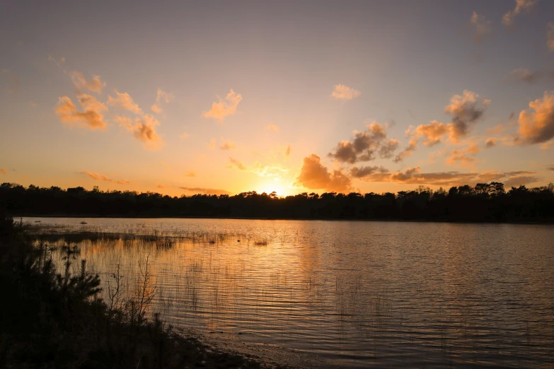 the sun rising over the lake in an orange sky