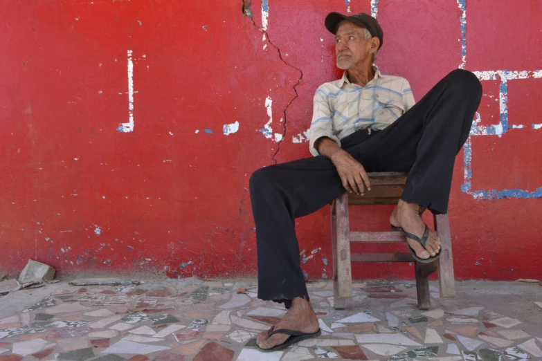 an old man sitting on a chair by a red wall