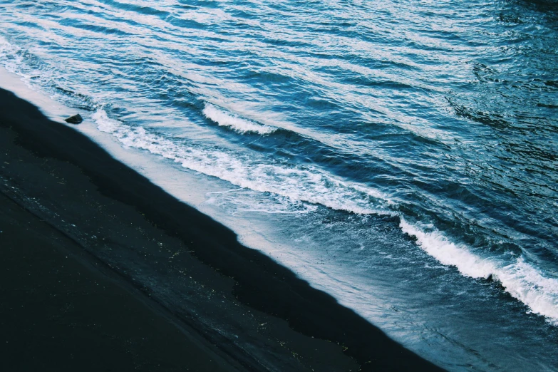 ocean waves coming into the shore in dark sand