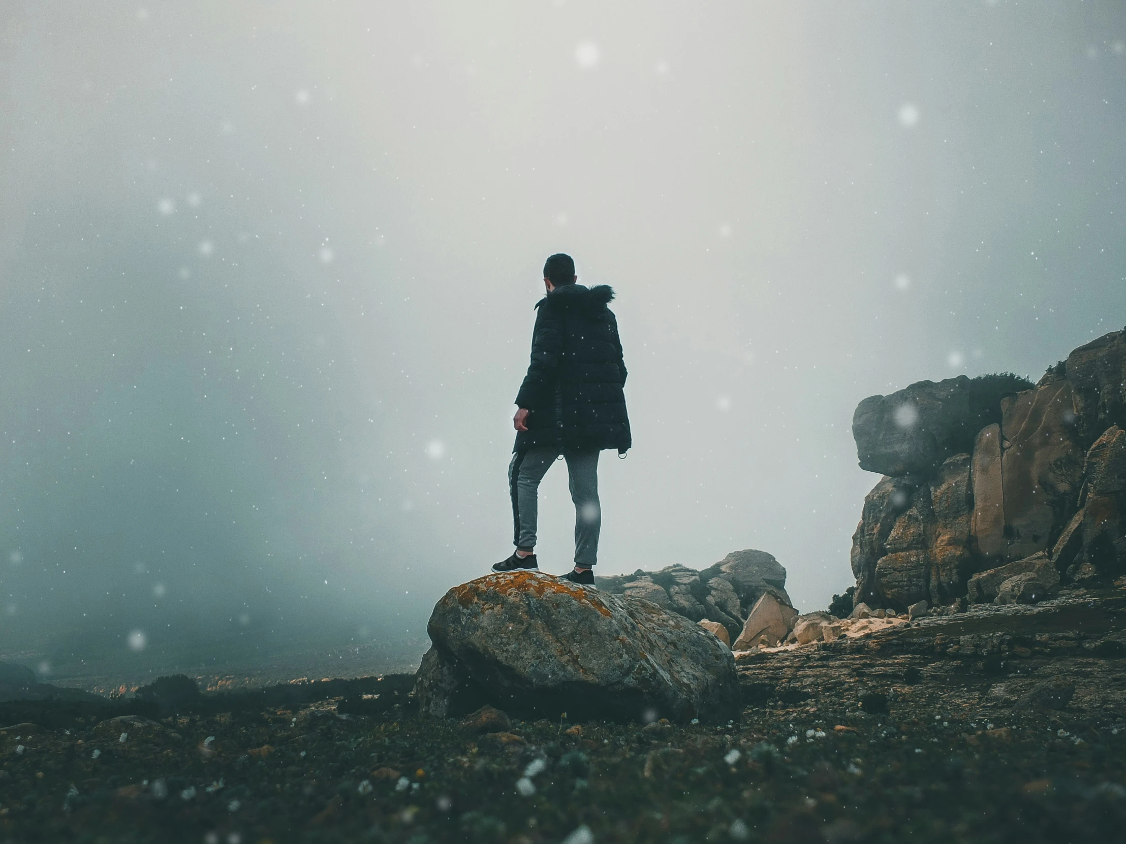 a man is standing on a rock alone in the midst of the snow