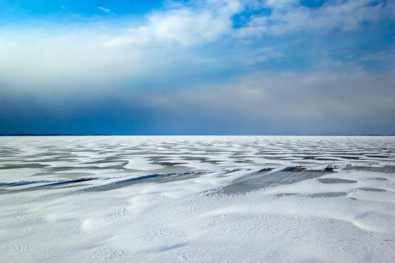 an empty field covered with snow under blue sky