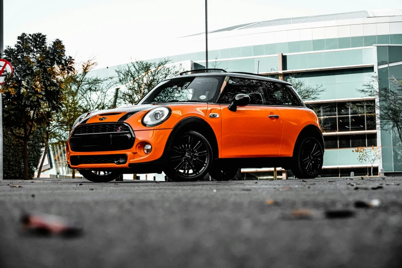 the front end of an orange mini cooper parked in front of a building