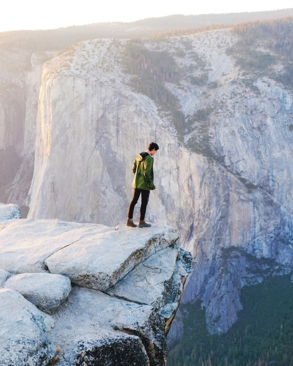 person standing on edge of cliff with backpack and looking out over valley below