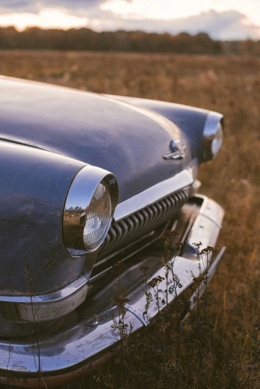 the old black car is parked on the dry grass