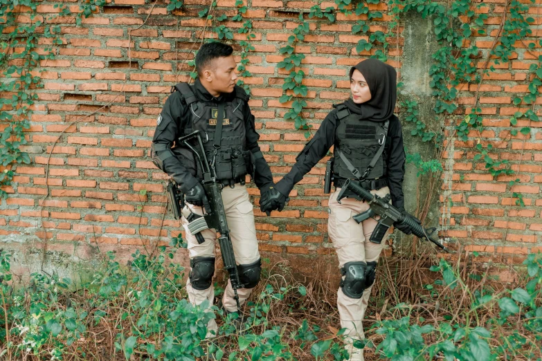 couple in full police uniforms holding hands while walking by brick wall
