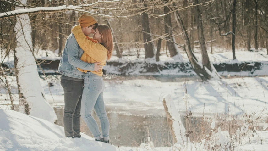 two people are kissing in the snow beside a stream