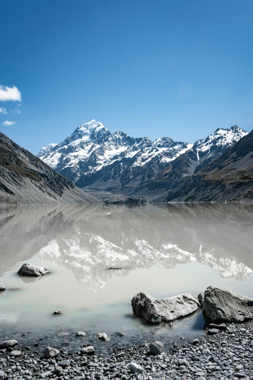 a view of snow capped mountains, some rocks and a body of water