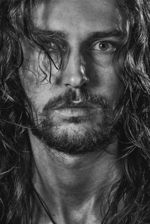 a man with long hair and beard standing in front of a black background