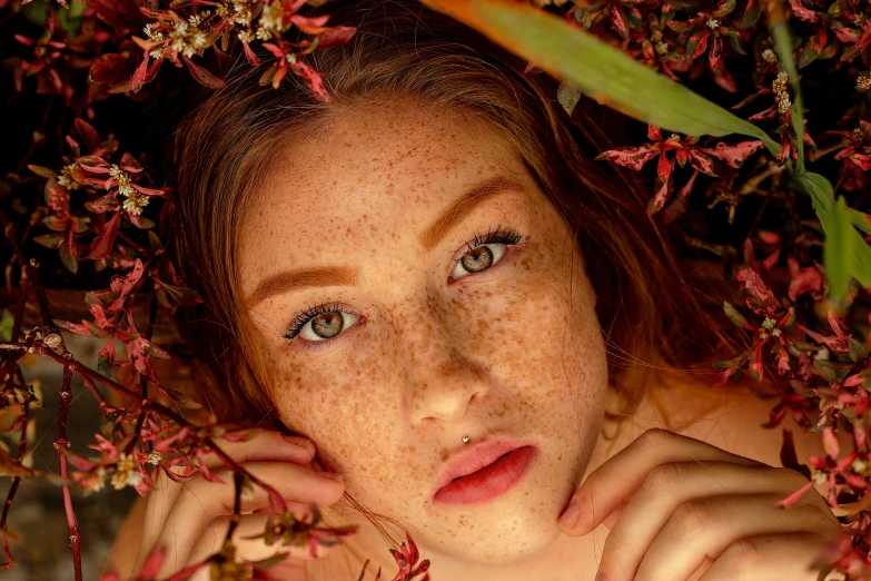 a girl with freckles on her face posing in front of some flowers