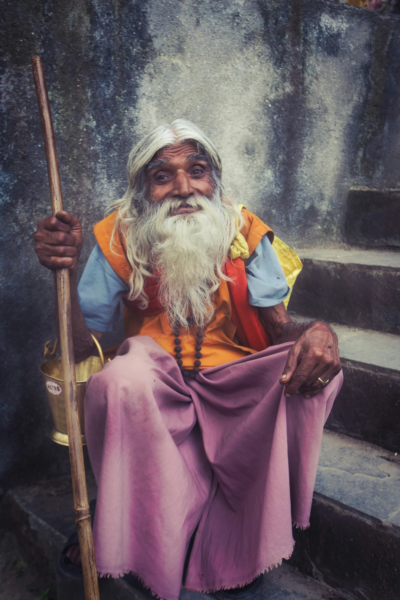 an old man in yellow sits and holds a stick