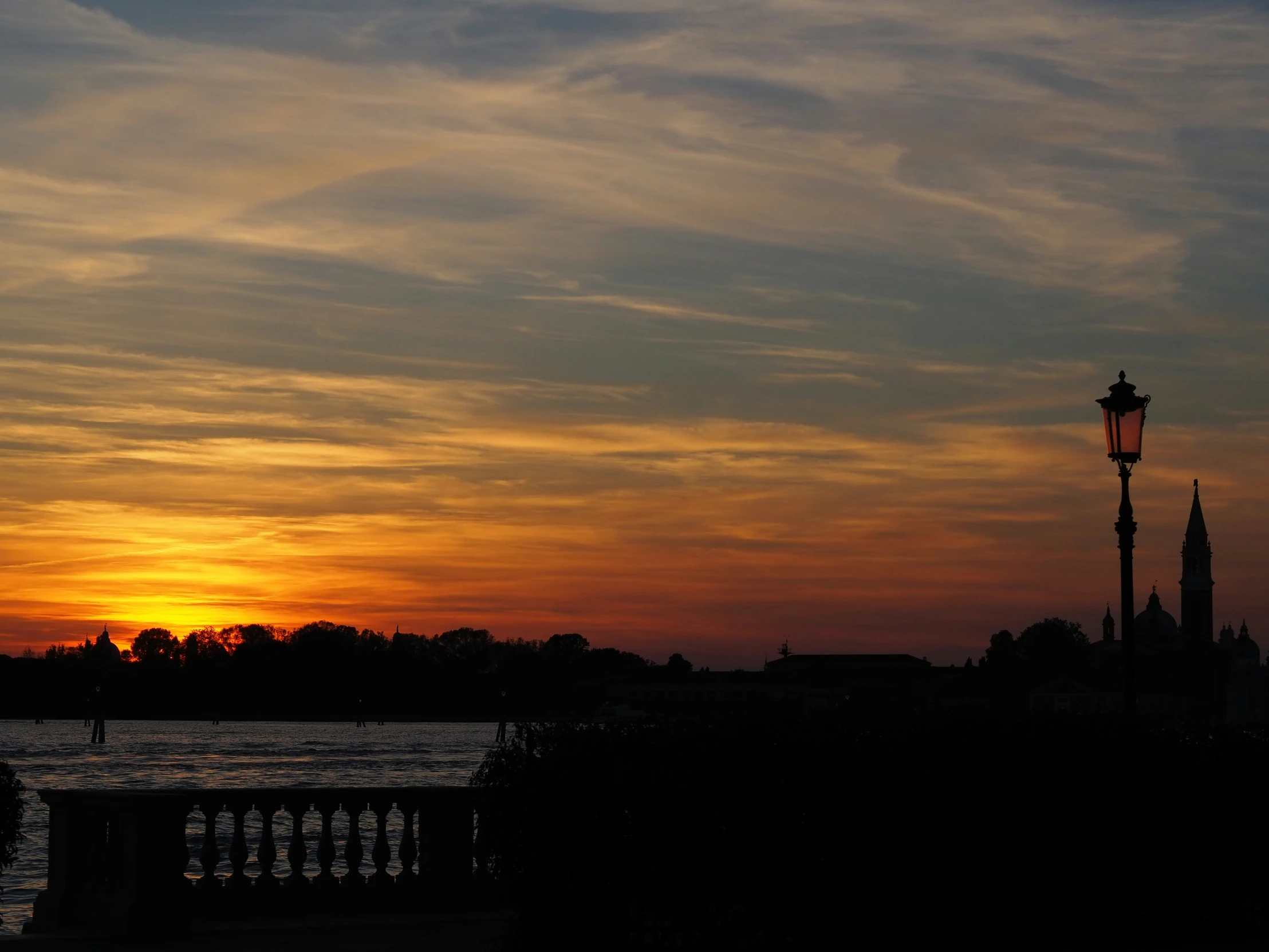 a picture of a sunset at a lake with a city in the background