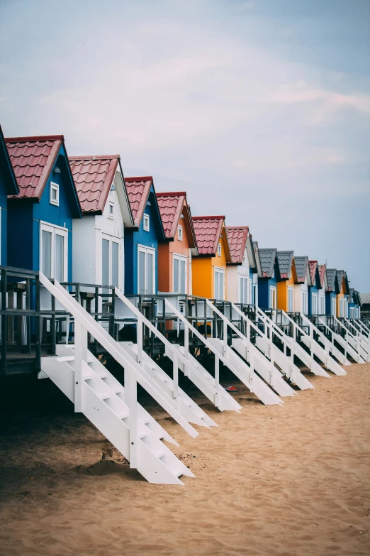 a row of colored beach huts sit on the beach