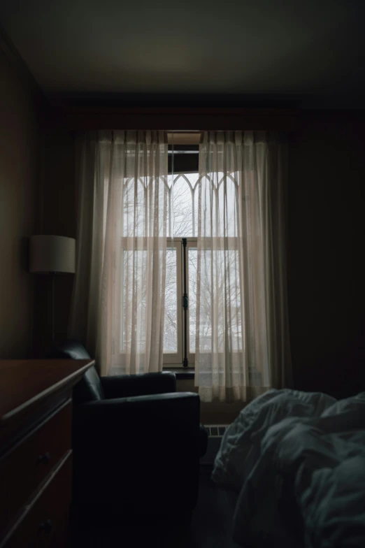 a dark bedroom with a bed, chair, and large window