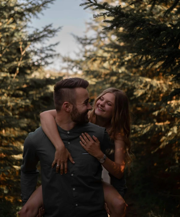 the couple is hugging in a wooded area while looking at each other