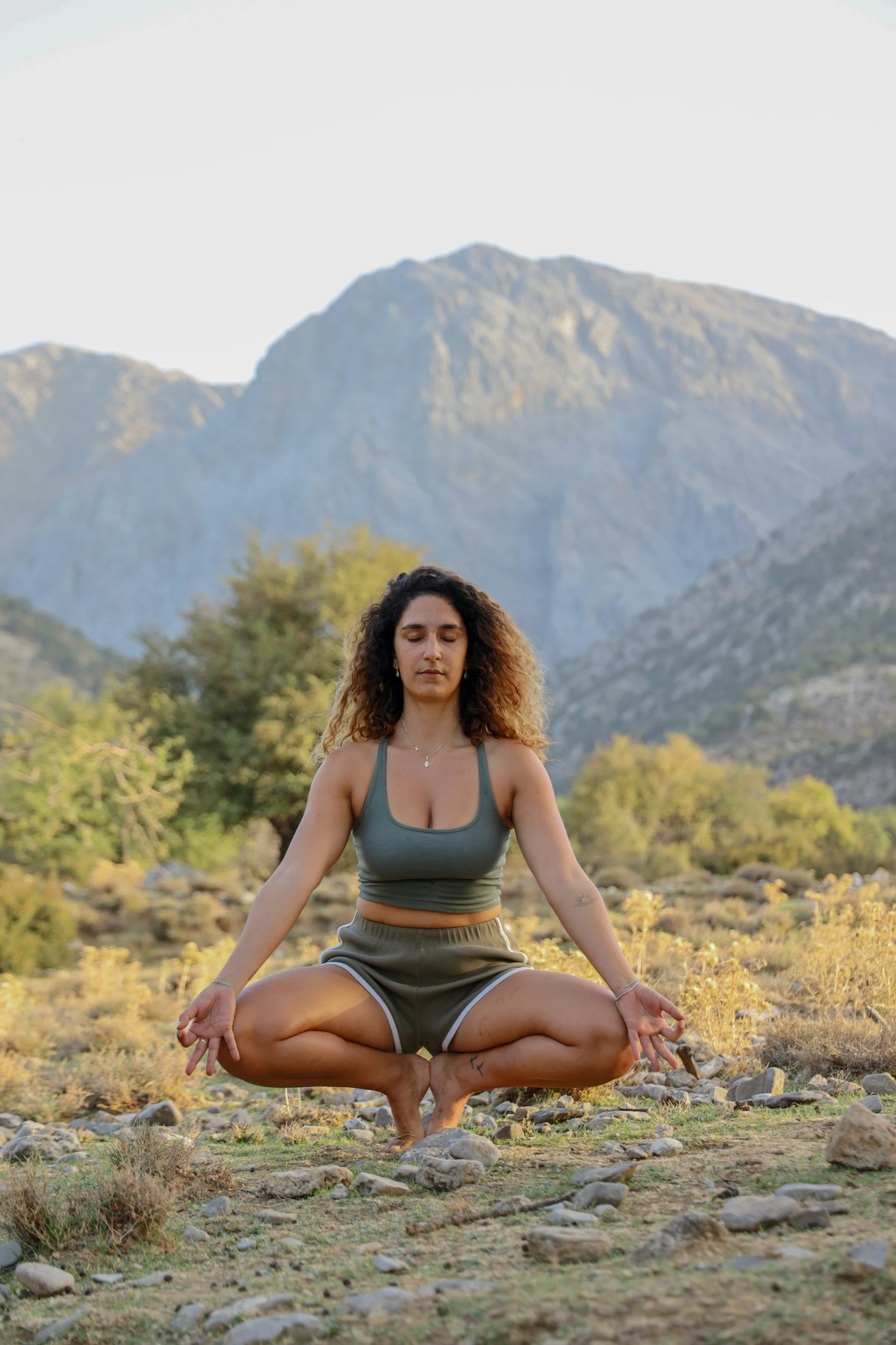 a beautiful woman sitting in the grass in front of some mountains