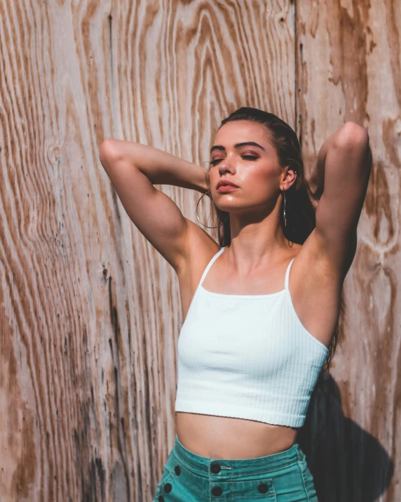 a woman wearing shorts and a top poses against a wooden wall