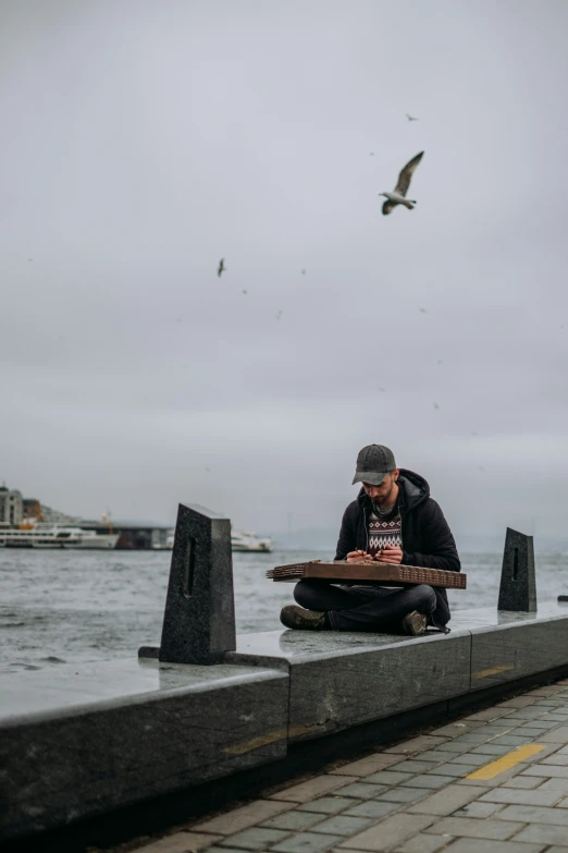 a man sitting on top of a concrete wall near a body of water