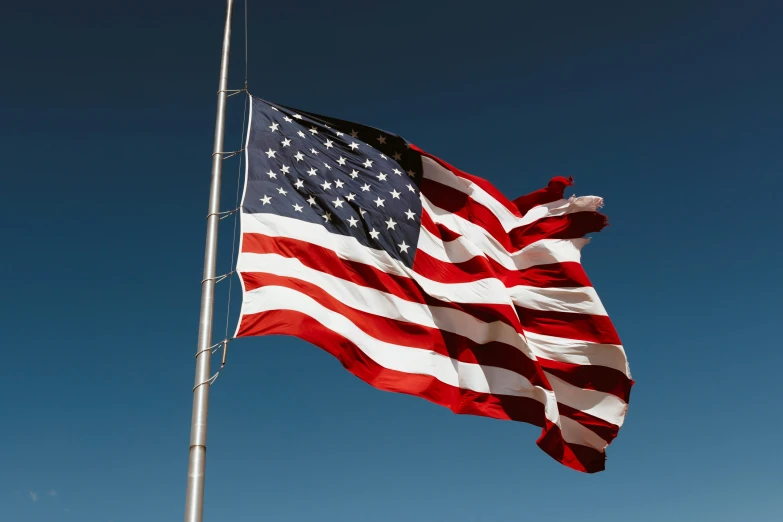 two large flags fly on a pole in front of blue sky