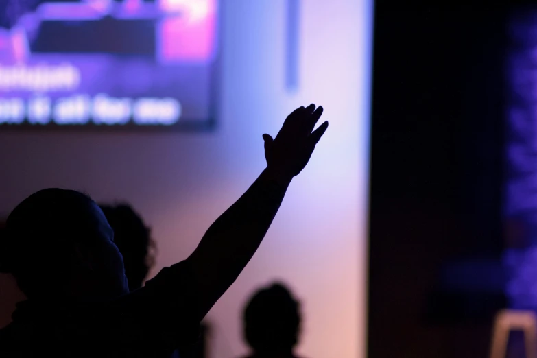 the silhouette of people at a conference raising their hands up