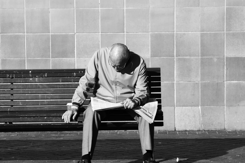 a man sits on a park bench reading a newspaper