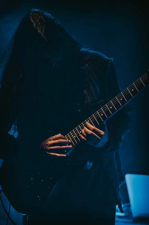 a man in black with long hair is playing a guitar