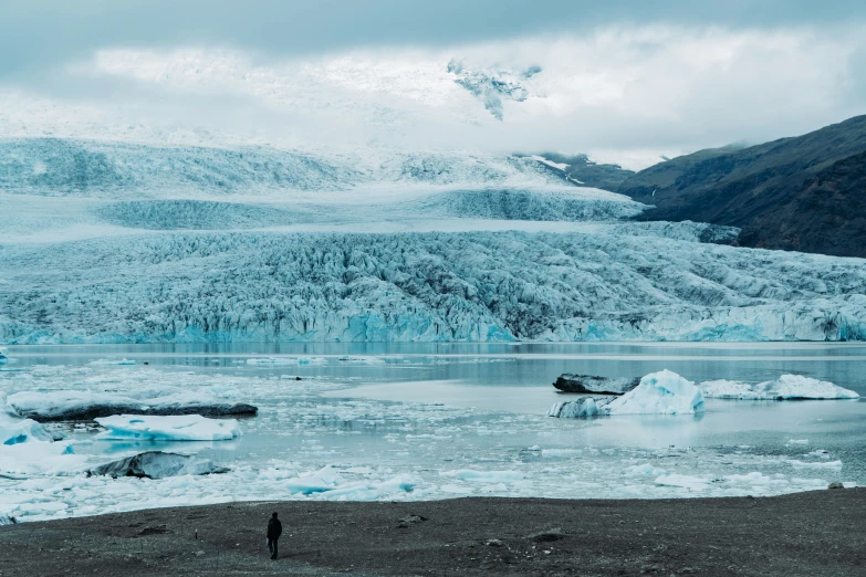 a man stands near water and glacier as he looks at it