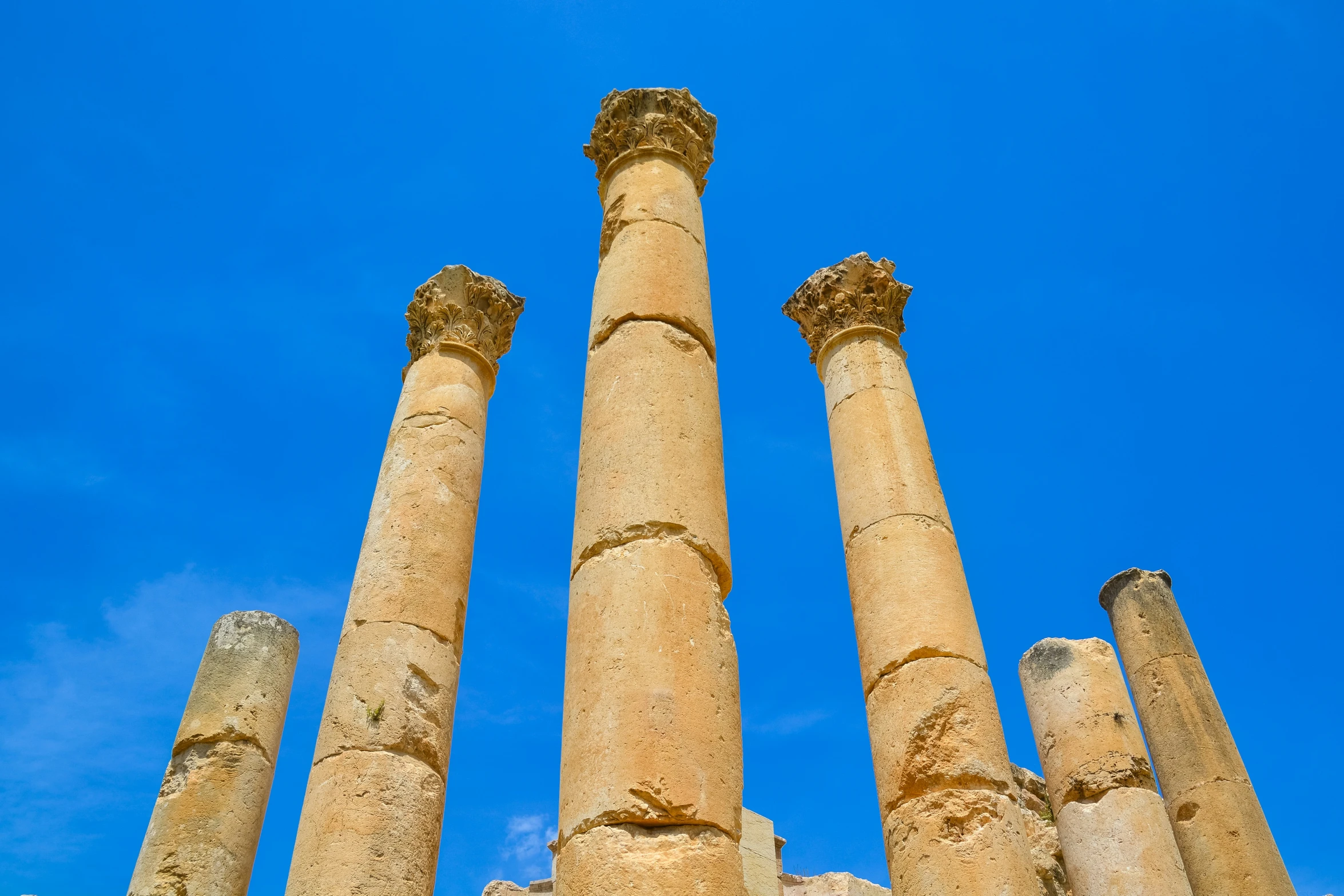 looking up at four ancient roman columns under a blue sky