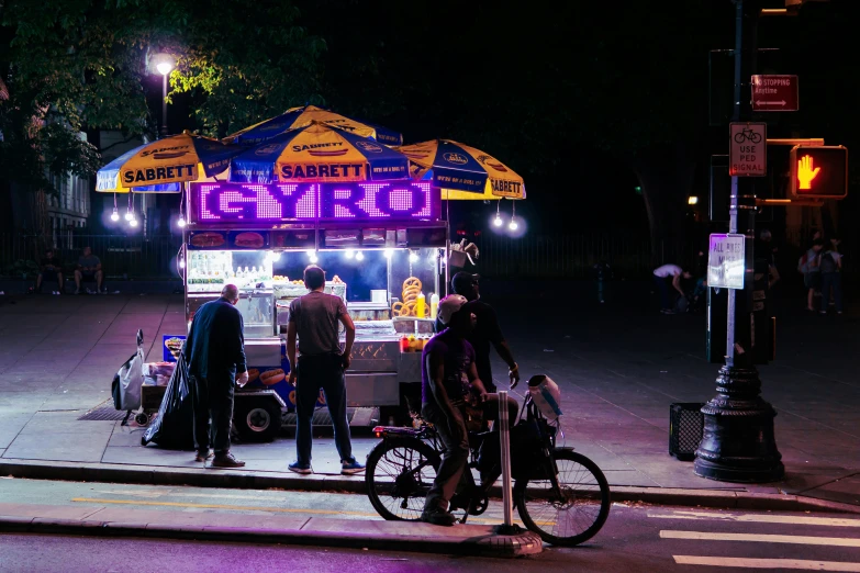 several people wait at a vendor stand in the street at night