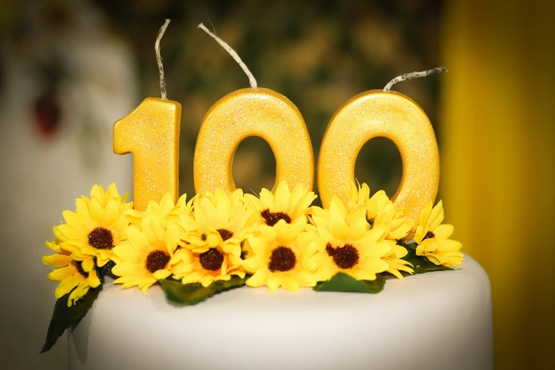 the number 100 is made of frosted candles with sunflowers on top