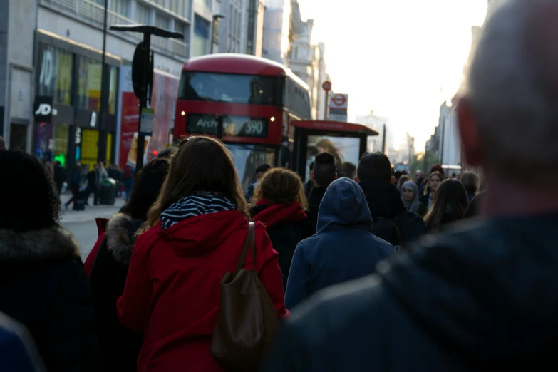 people stand on the side walk watching a double decker bus