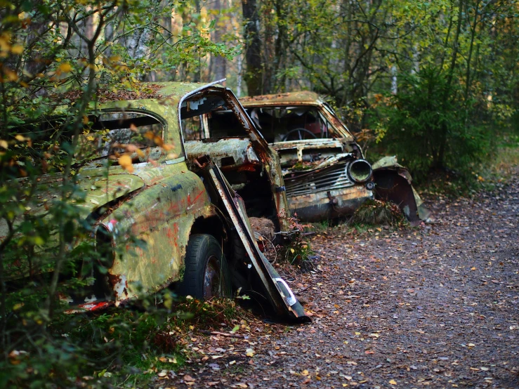 an old car in the forest on the side of the road