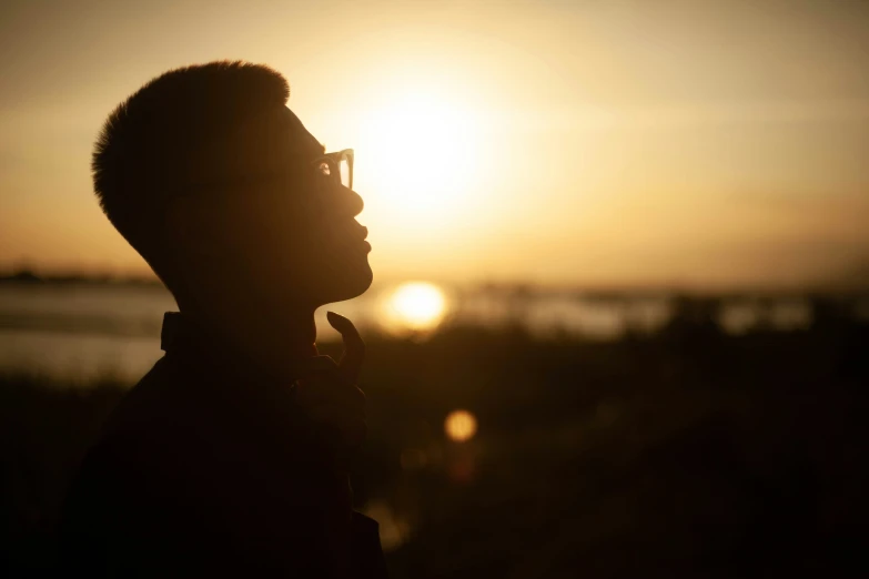 a man wearing glasses is silhouetted against a sun set