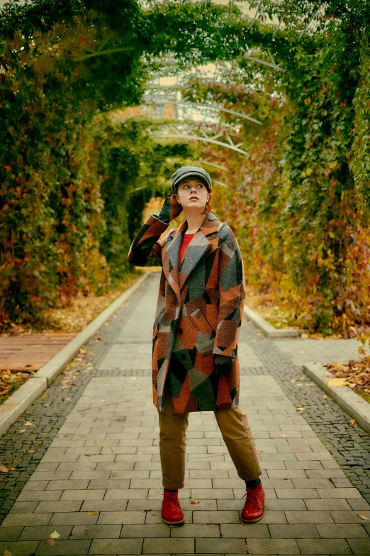 a man standing on a path in a park wearing a jacket and a hat