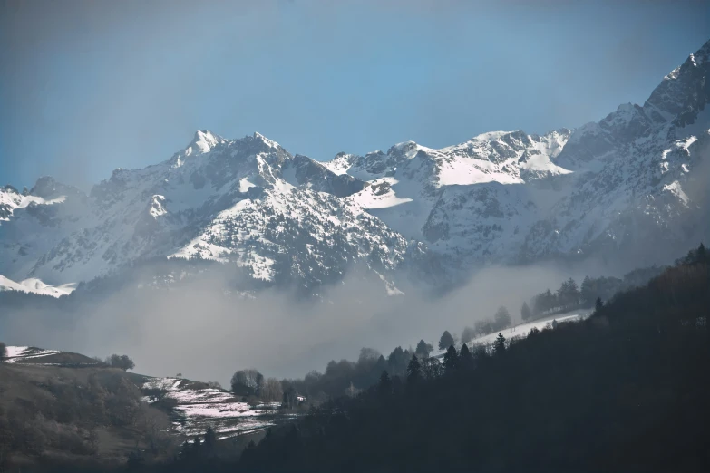 a snow covered mountain range with low clouds