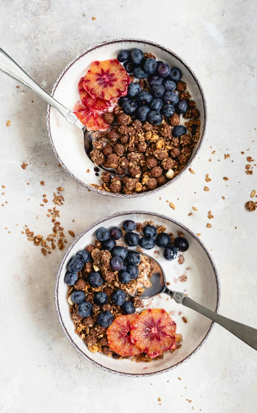 two bowls of cereal, fruit and milk sit on a table