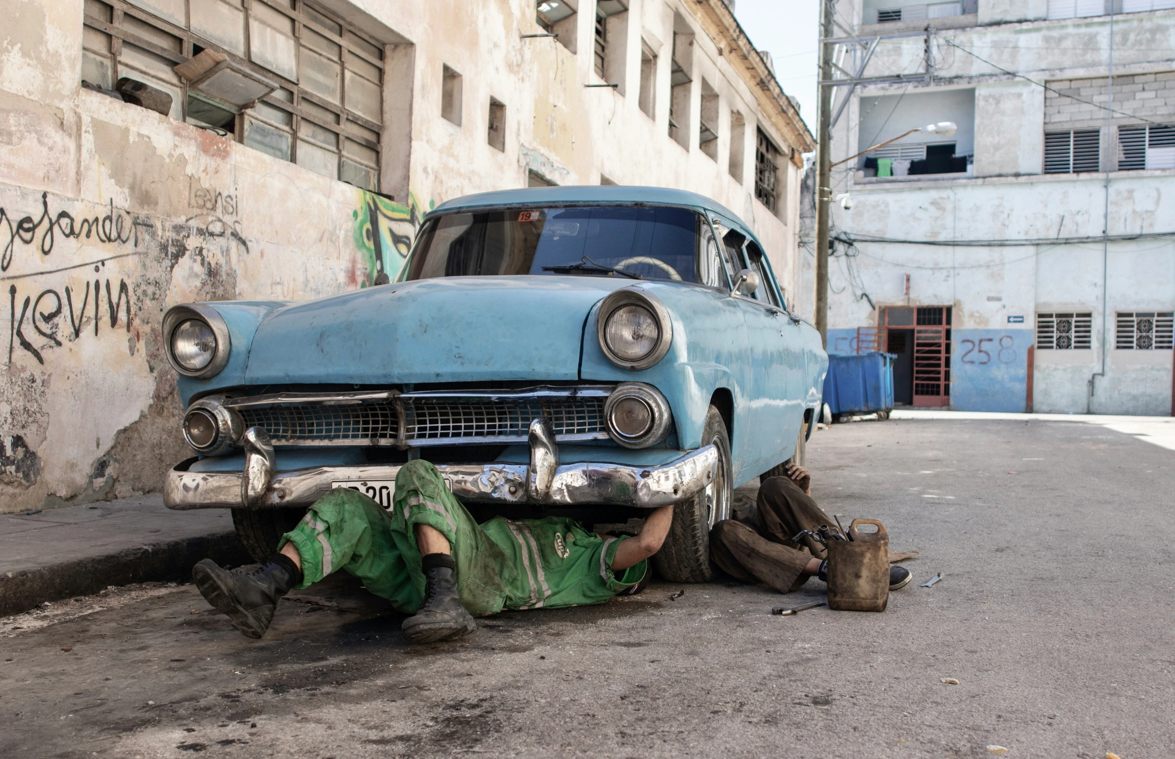 a man sits on his feet on the ground while looking at a broken up car