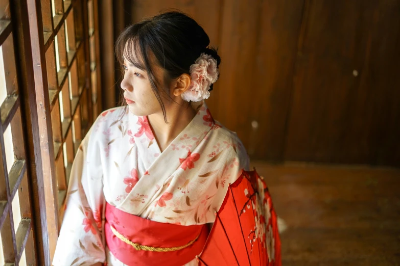 an asian woman in a kimono stands by a window