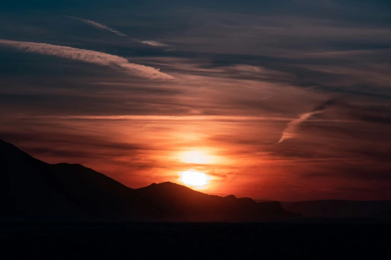 a sun sets over mountains and hills in the distance