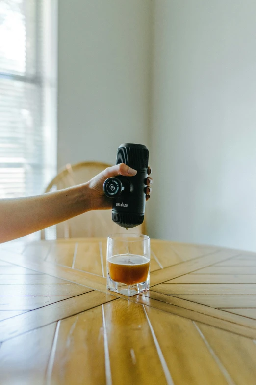 a hand holding a camera over a glass with a beer in it