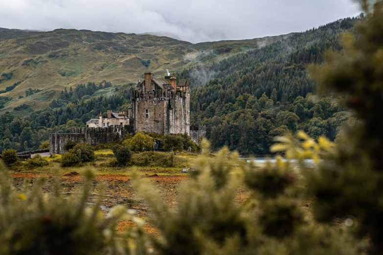 an old castle sitting on top of a mountain surrounded by forest