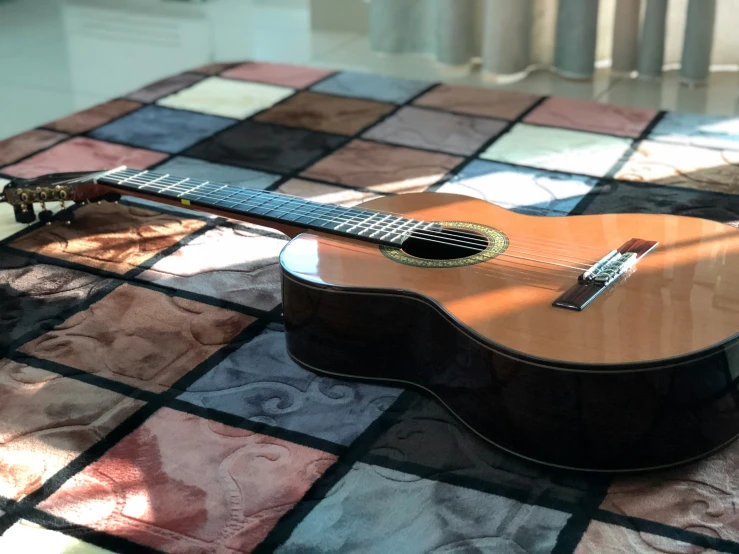 a small guitar is laying on a rug and a window