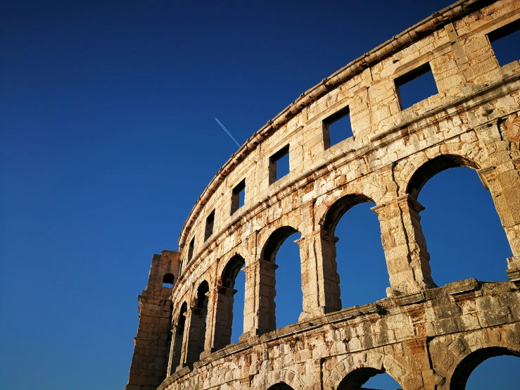 an ancient stone building with a jet flying in the background