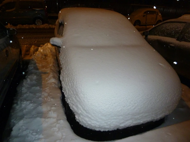 a snow covered car on a sidewalk in the night