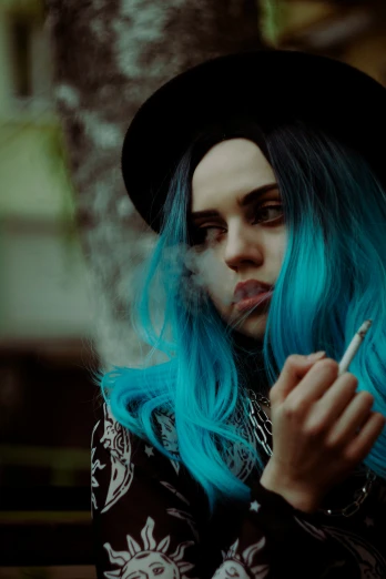 a man wearing a hat and blue hair smoking a cigarette