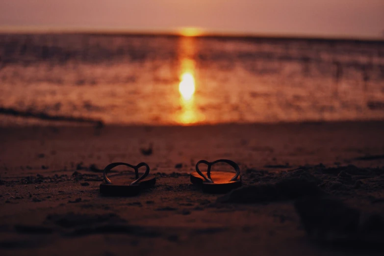 two pairs of sandals sitting in the sand by the water