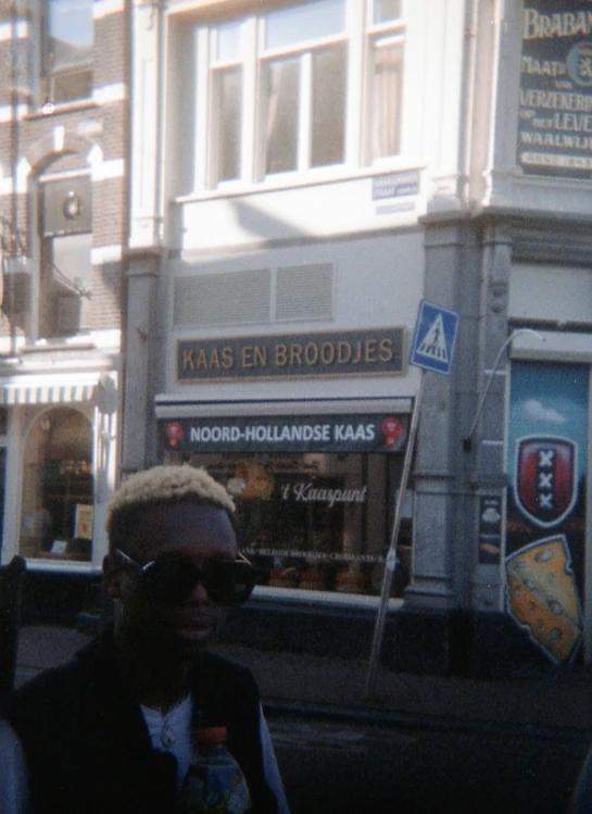 a man in a black vest and dark sunglasses stands outside of a shop