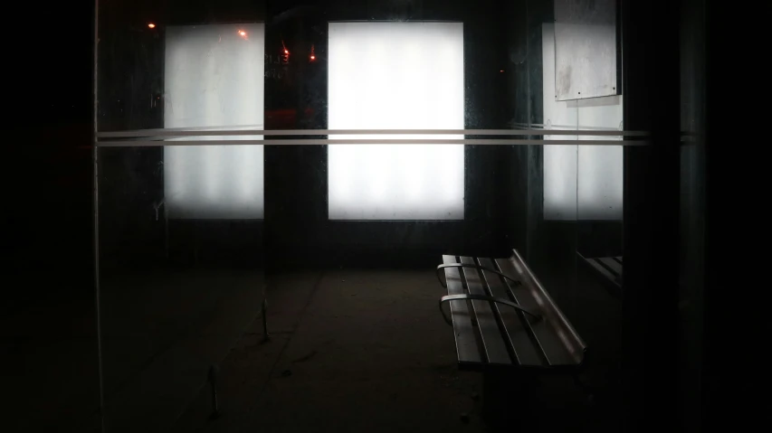 a park bench sitting in a dark spot with sunlight coming through the window